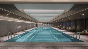 A long indoor swimming pool with a modern design, surrounded by seating areas and a high ceiling.