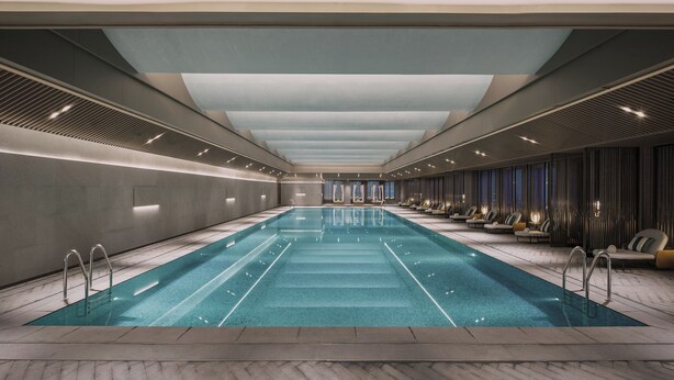 Ein langer, innenliegender Schwimmbereich mit modernem Design, umgeben von Sitzgelegenheiten und einer hohen Decke.