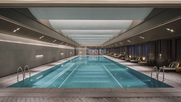 A long indoor swimming pool with a modern design, surrounded by seating areas and a high ceiling.