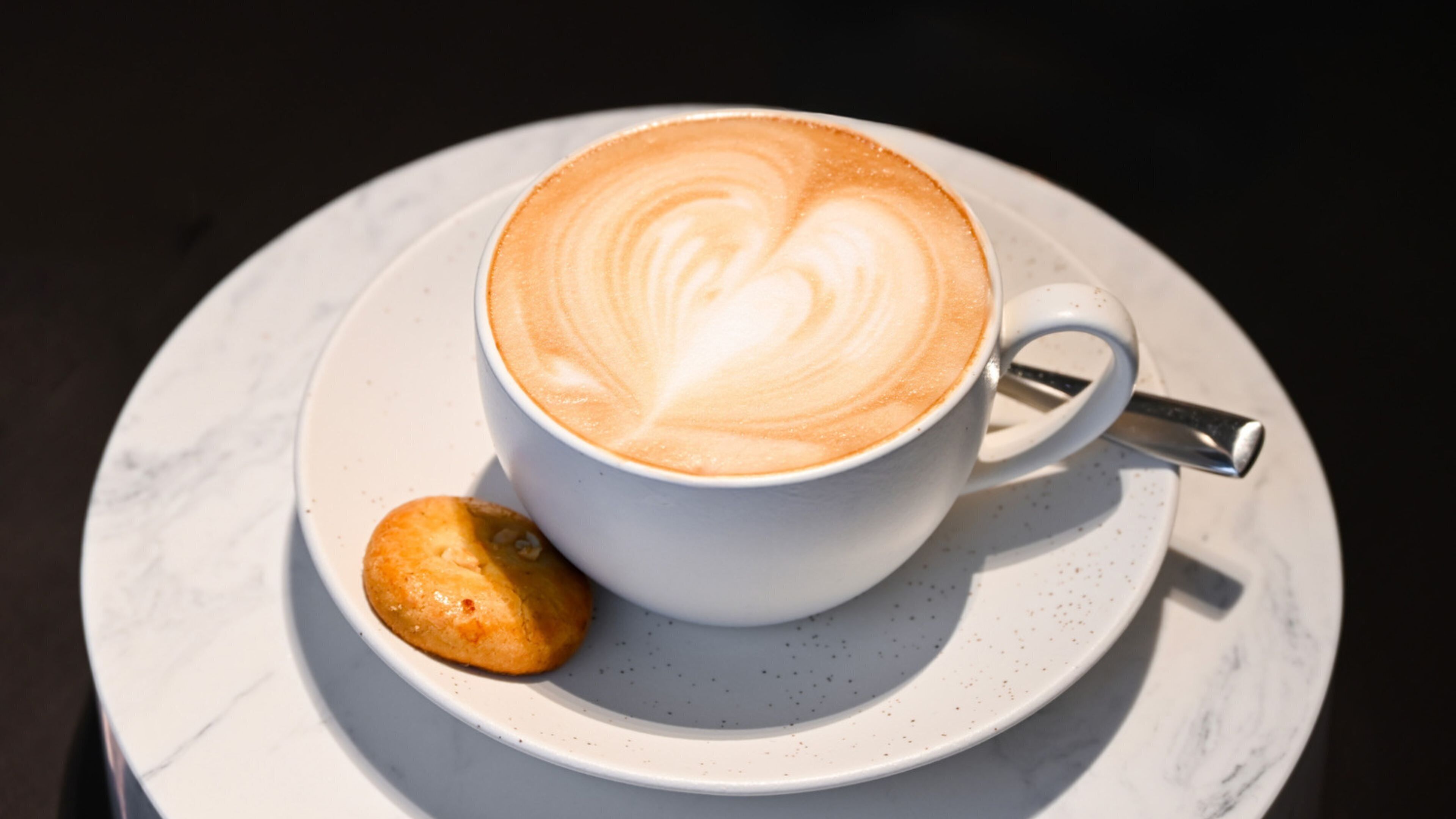 Eine Tasse Kaffee mit Latte-Art auf einem Untertasse, dazu ein Keks.