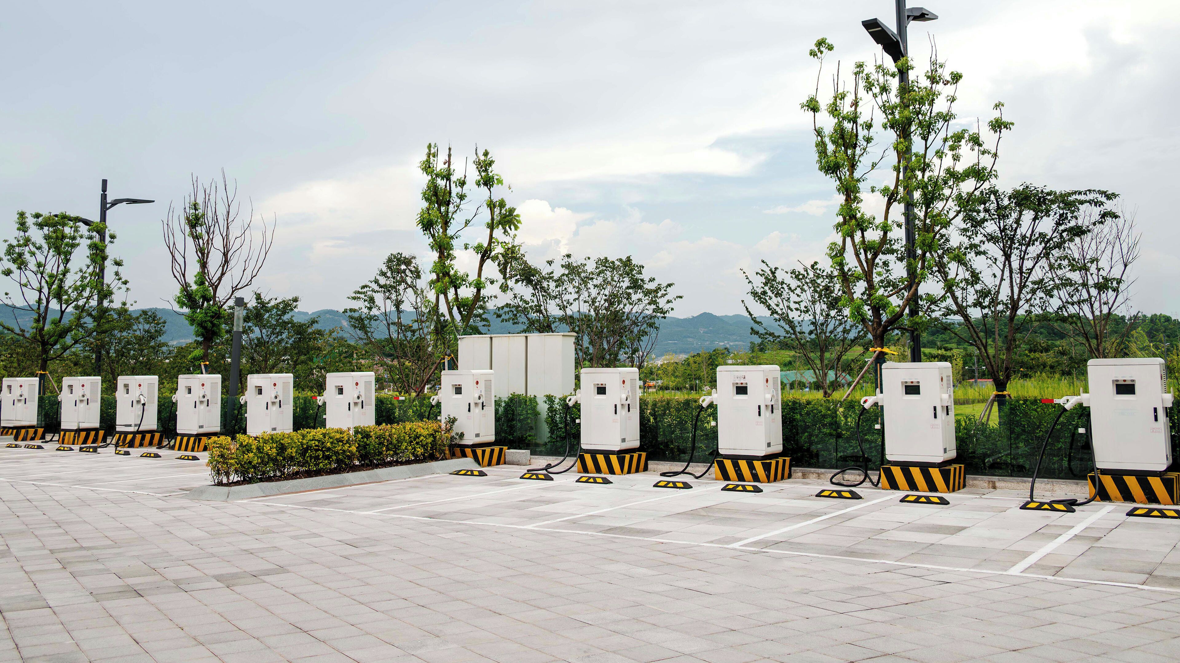 Un espace de stationnement équipé de bornes de recharge pour véhicules électriques, entouré d’arbres et avec un paysage montagneux en arrière-plan.