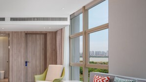 A modern hotel room with a large window offering a city view, a seating area with a table, and a door with a blue sign. - Holiday Inn Express Nanchang High Tech Zone by IHG (Nanchang)