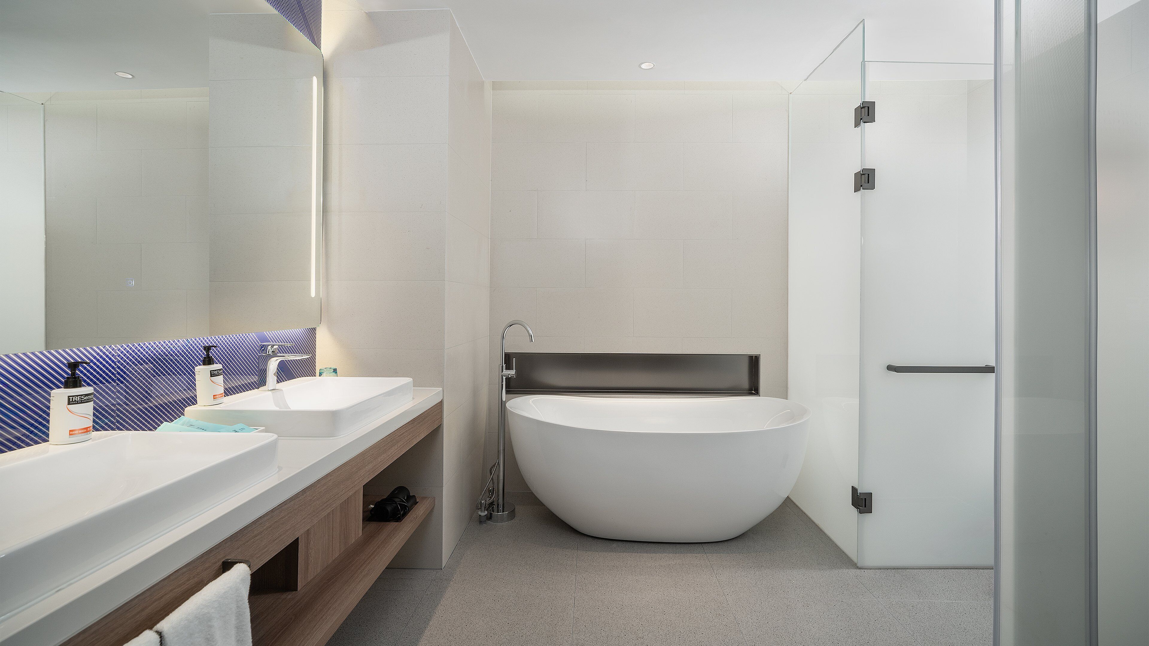 Un baño moderno con una bañera independiente, un espejo grande y un tocador con dos lavamanos.
