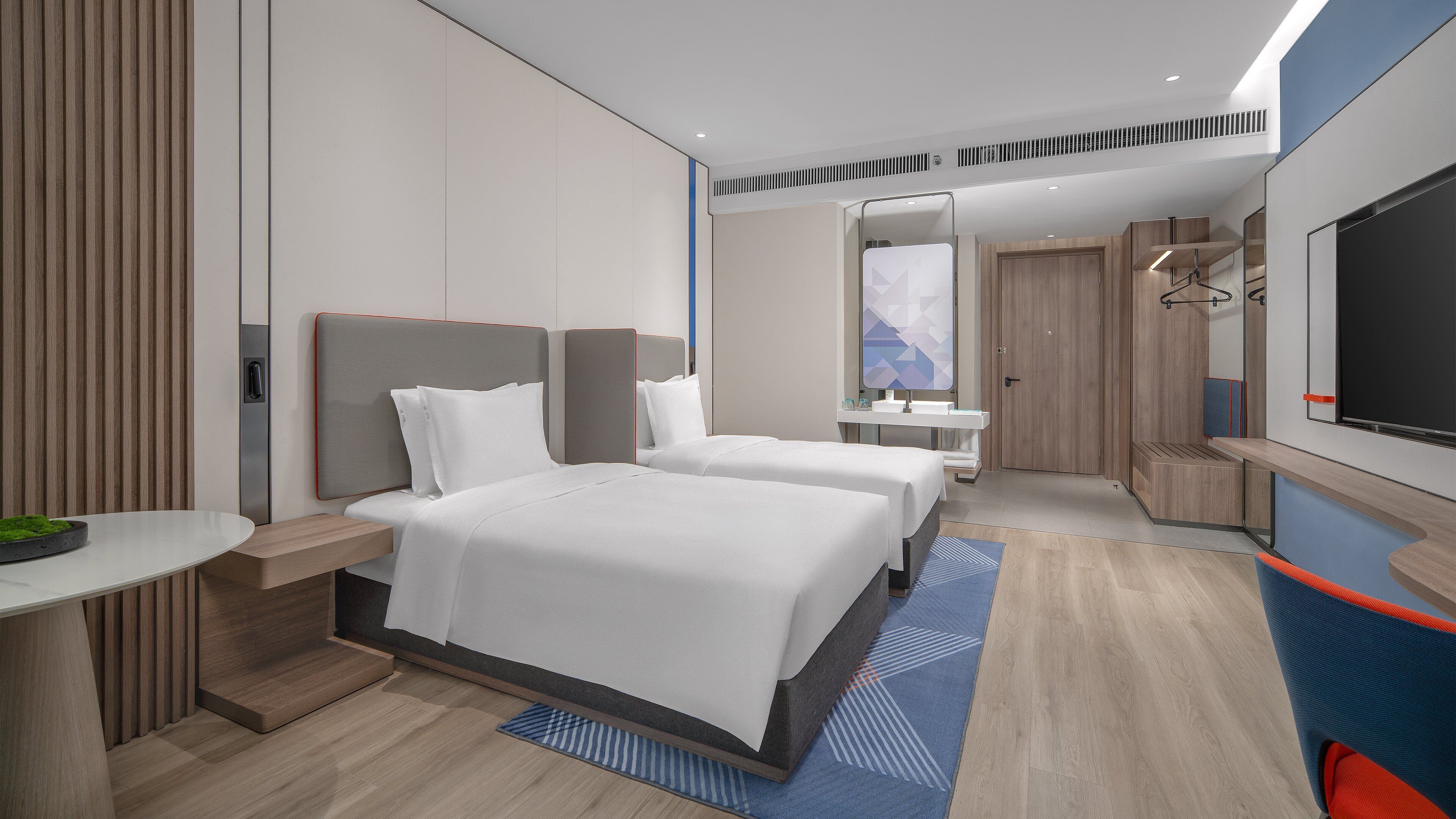 A modern hotel room with two beds, a desk, a bathroom, and a TV.