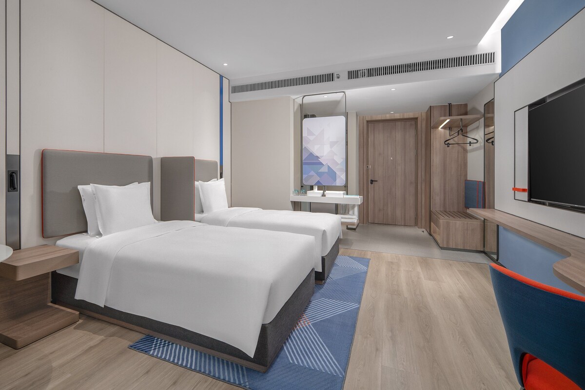 A modern hotel room with two beds, a desk, a bathroom, and a TV.