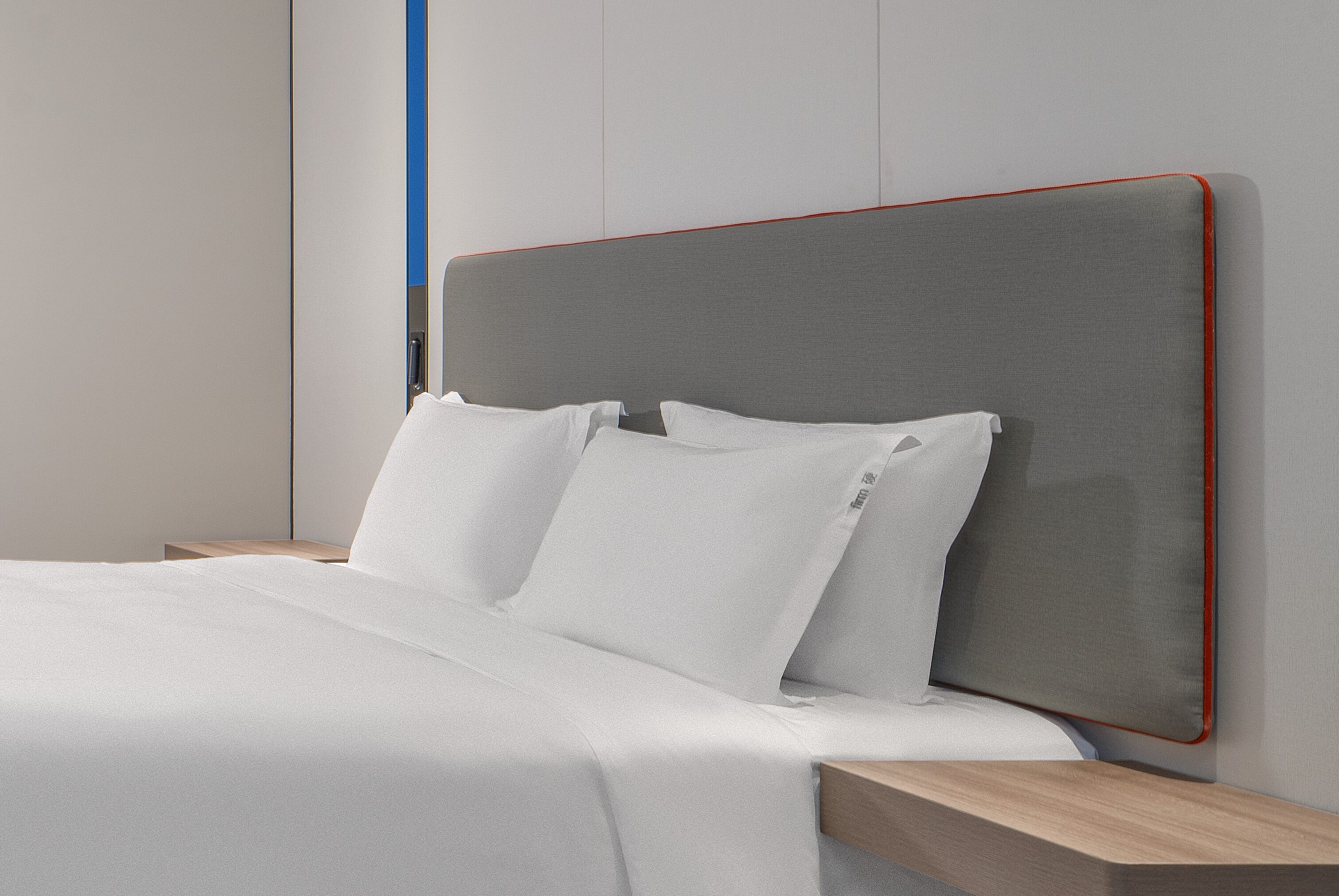 Ein modernes Schlafzimmer mit grauem Kopfteil, weißer Bettwäsche und einem Nachttisch aus Holz.