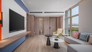A modern living room with a flat-screen TV, a round coffee table, a sofa with patterned cushions, and a large window offering a city view. - Holiday Inn Express Nanchang High Tech Zone by IHG (Nanchang)