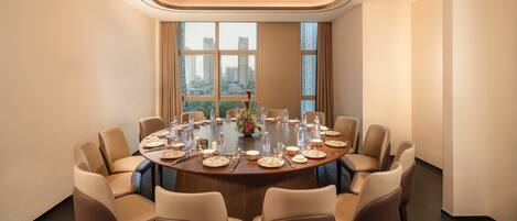 A conference room with a round table, beige chairs, and a city view through large windows.