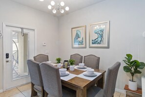 Een eethoek met een houten tafel, grijs gestoffeerde stoelen, witte borden en twee ingelijste kunstwerken aan de muur.