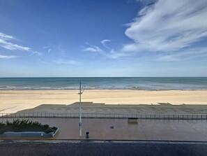 Blick auf einen Strand mit gepflastertem Weg, einem Laternenpfahl und einer Bank.