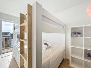Ein modernes Schlafzimmer mit Etagenbett, einem Balkon mit Aussicht und einem weißen Regal.