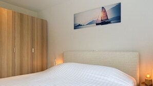 Een slaapkamer met een bed, een kledingkast, een nachtkastje en een aan de muur hangend schilderij.