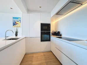 Une cuisine moderne avec des meubles blancs, un four encastré et un évier.