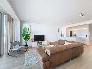 A modern living room with a brown leather sofa, a grey chair, a TV, and a large plant.