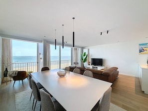 Una sala de estar moderna con comedor, televisor y vista al mar.