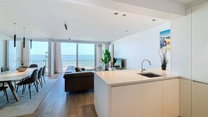 Een moderne keuken met een centraal eiland, een eethoek met een tafel en stoelen, een bank en uitzicht op de oceaan.