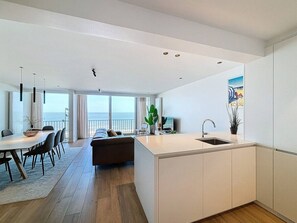 Une cuisine moderne avec un îlot central, un coin repas comprenant une table et des chaises, un canapé et une vue sur l’océan.