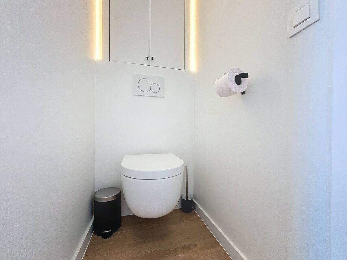 A small, modern bathroom with a white toilet, a trash bin, and a toilet paper holder.