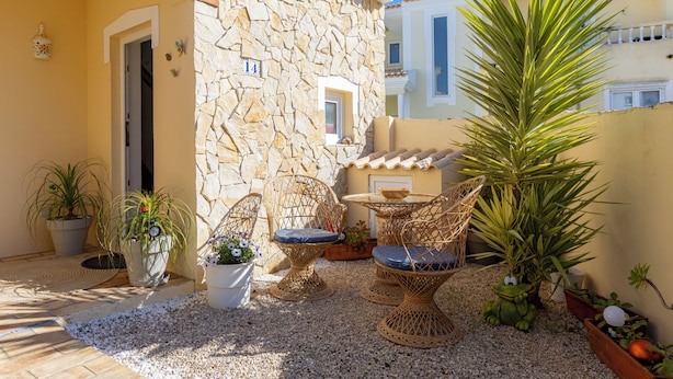 Un patio con mobiliario de mimbre, plantas en macetas y un muro de piedra.