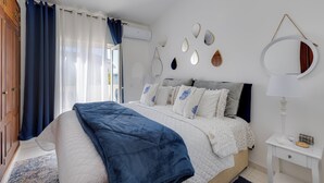 Un dormitorio con cama, cortinas, una mesita de noche con lámpara y adornos en la pared.
