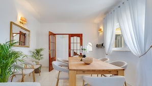 Un comedor con mesa de madera, sillas blancas, plantas en macetas y un espejo en la pared.