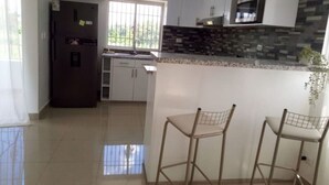 Cozinha moderna com armários brancos, geladeira preta, painel de azulejos e dois banquetas.