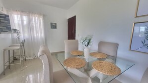 Uma área de jantar com mesa de vidro, jogos americanos trançados e um vaso de flores.