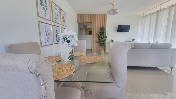 Uma sala de estar moderna com uma mesa de centro de vidro, sofás bege e impressões botânicas emolduradas na parede.