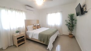 Quarto com cama, mesa de cabeceira, planta em vaso e ventilador de teto.