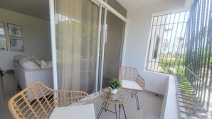 Uma varanda com móveis de vime, uma mesa pequena com uma planta e vista para o exterior.