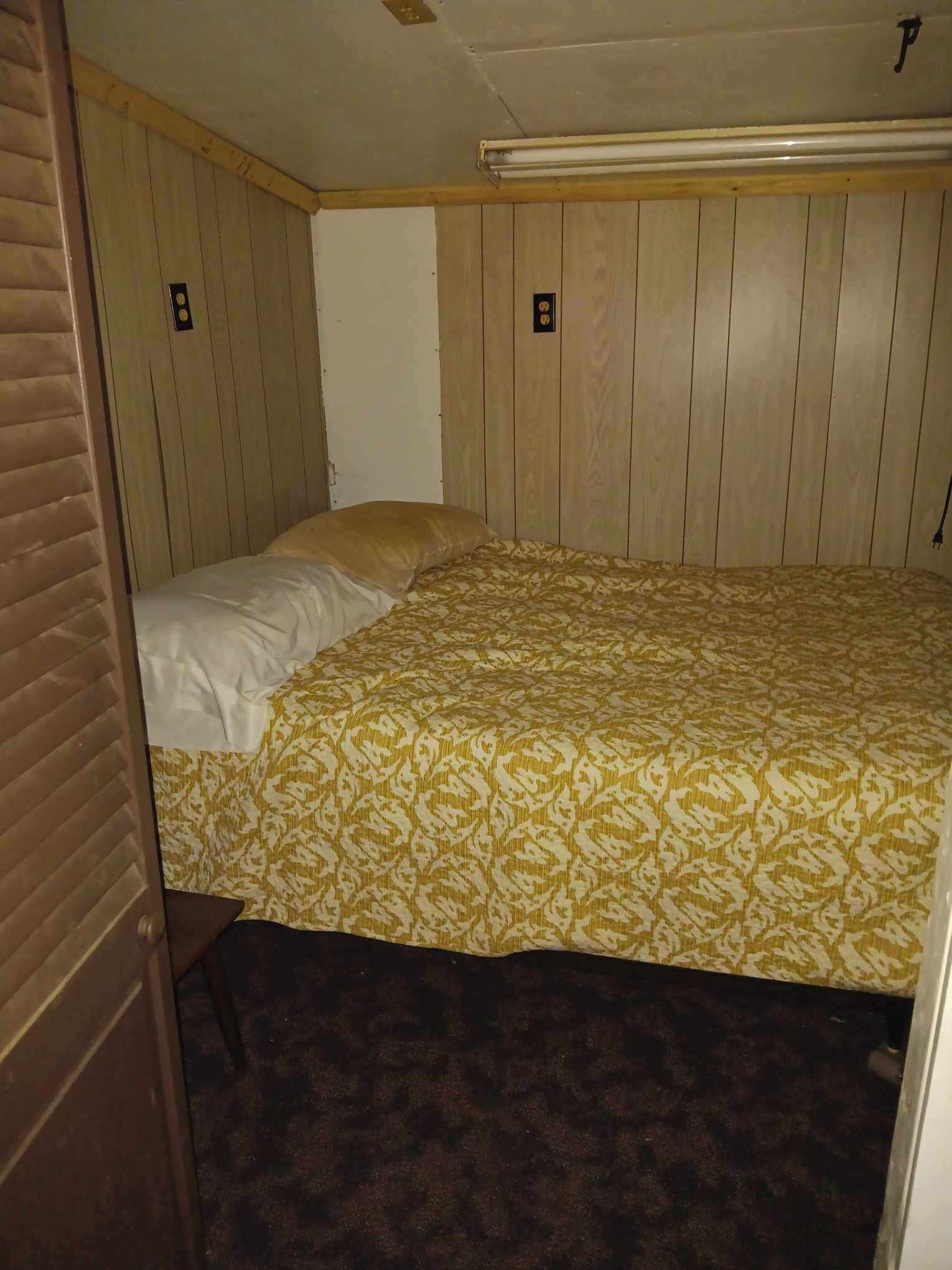 Een kleine eenpersoonskamer met houten paneelwanden, een bed met een decoratief sprei en een vloerbedekking.