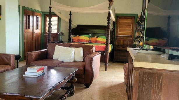 A traditional room with a four-poster bed, a leather sofa, a wooden coffee table, and a television. - Lion Farm's Eco Villas in 9 Mile Jamaica with Mountain View’s  (Nine Mile)