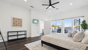 A bedroom with a large bed, a ceiling fan, a TV, and a window with a view of buildings. - The Terrace In Dallas I Downtown Dallas I House (Dallas)