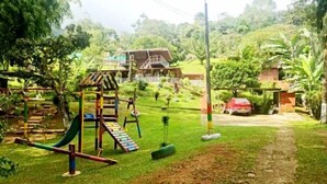 A playground with swings and a slide, surrounded by greenery and a house in the background. - finca ecoturistica el paraiso (Cali)