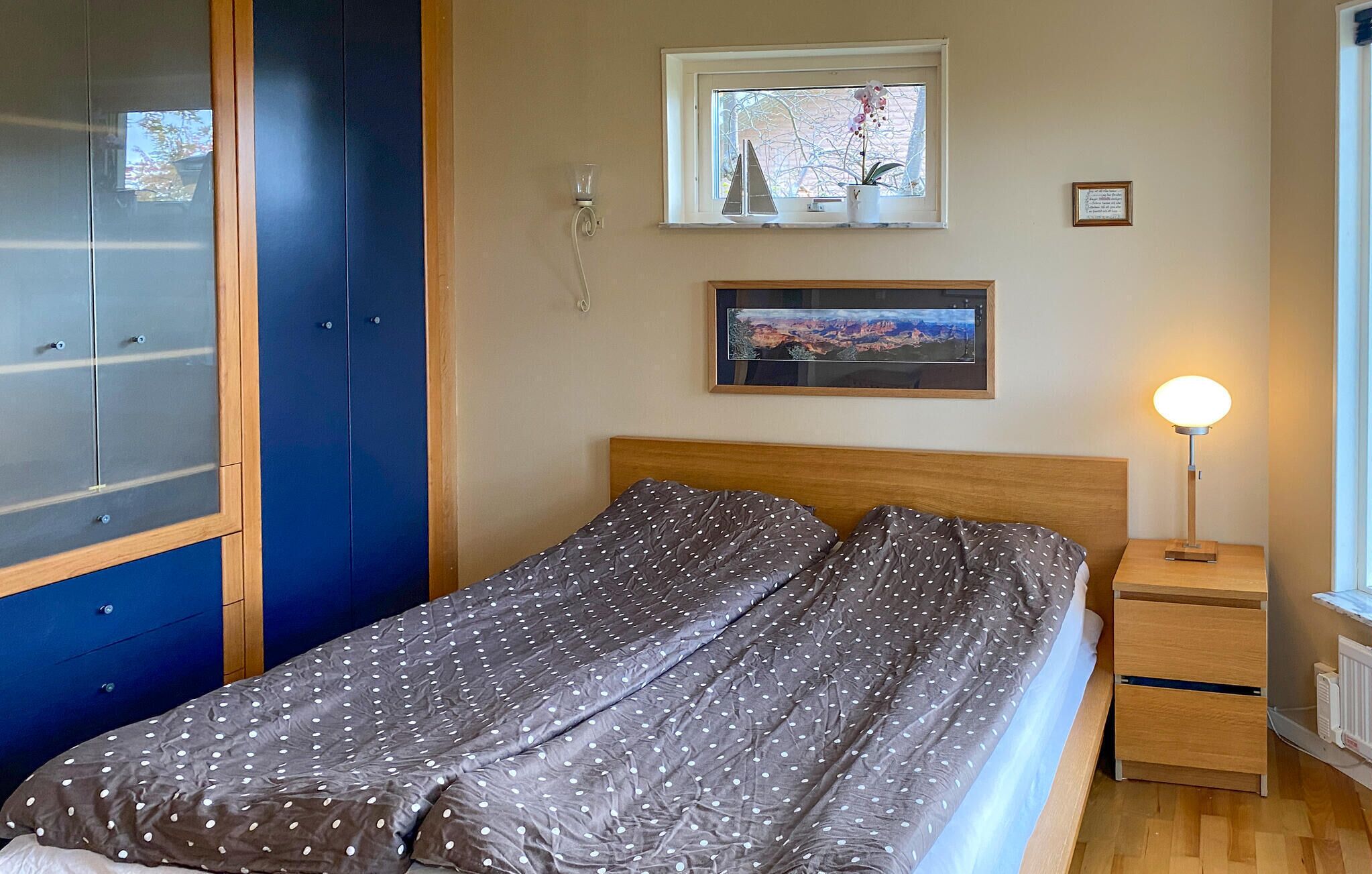 Een slaapkamer met een bed, nachtkastje, lamp, raam met uitzicht en een kledingkast.