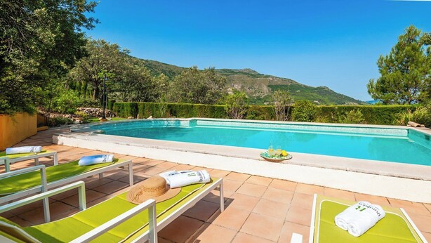 A poolside area with lounge chairs, a sunshade, and a tray with drinks and lemons.