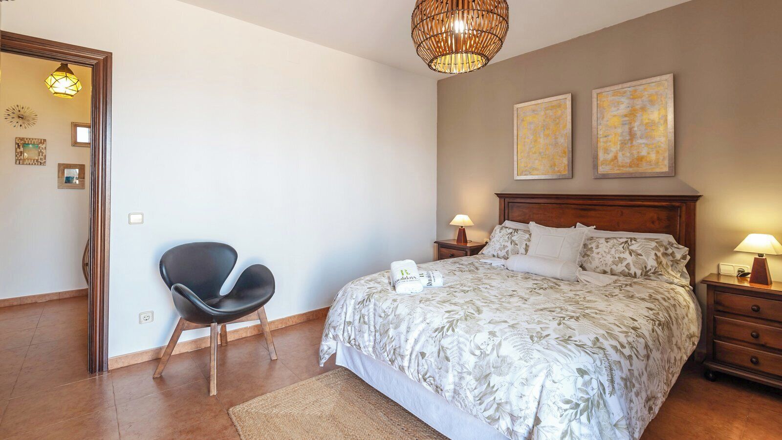 A bedroom with a bed, a chair, a nightstand, and two wall-mounted lamps.