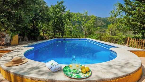A swimming pool with a stone deck, surrounded by lush greenery and hills. - Azuara 3 Dormitorios Los Villares by Ruralidays (Jaén)