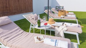 Un espace de détente extérieur, baigné de soleil, avec des fauteuils inclinables, une table sur laquelle se trouvent une bouteille de champagne, des verres et un saladier rempli de fruits.
