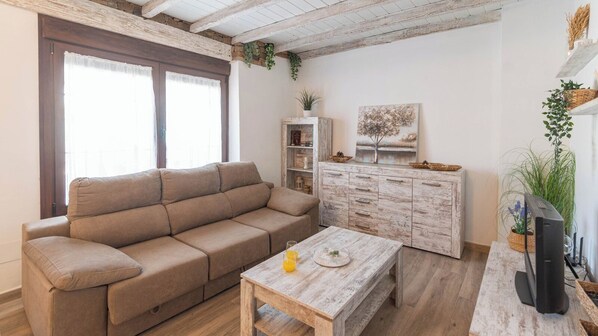Een gezellige woonkamer met een beige bank, een houten salontafel en een rustieke kast.