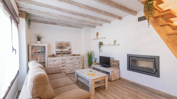 Un salon chaleureux avec un canapé, une table basse, un téléviseur, une cheminée et des étagères en bois ornées de plantes.