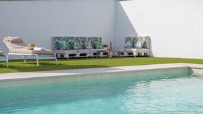 Une piscine avec des chaises longues et un petit espace aménagé en jardin.