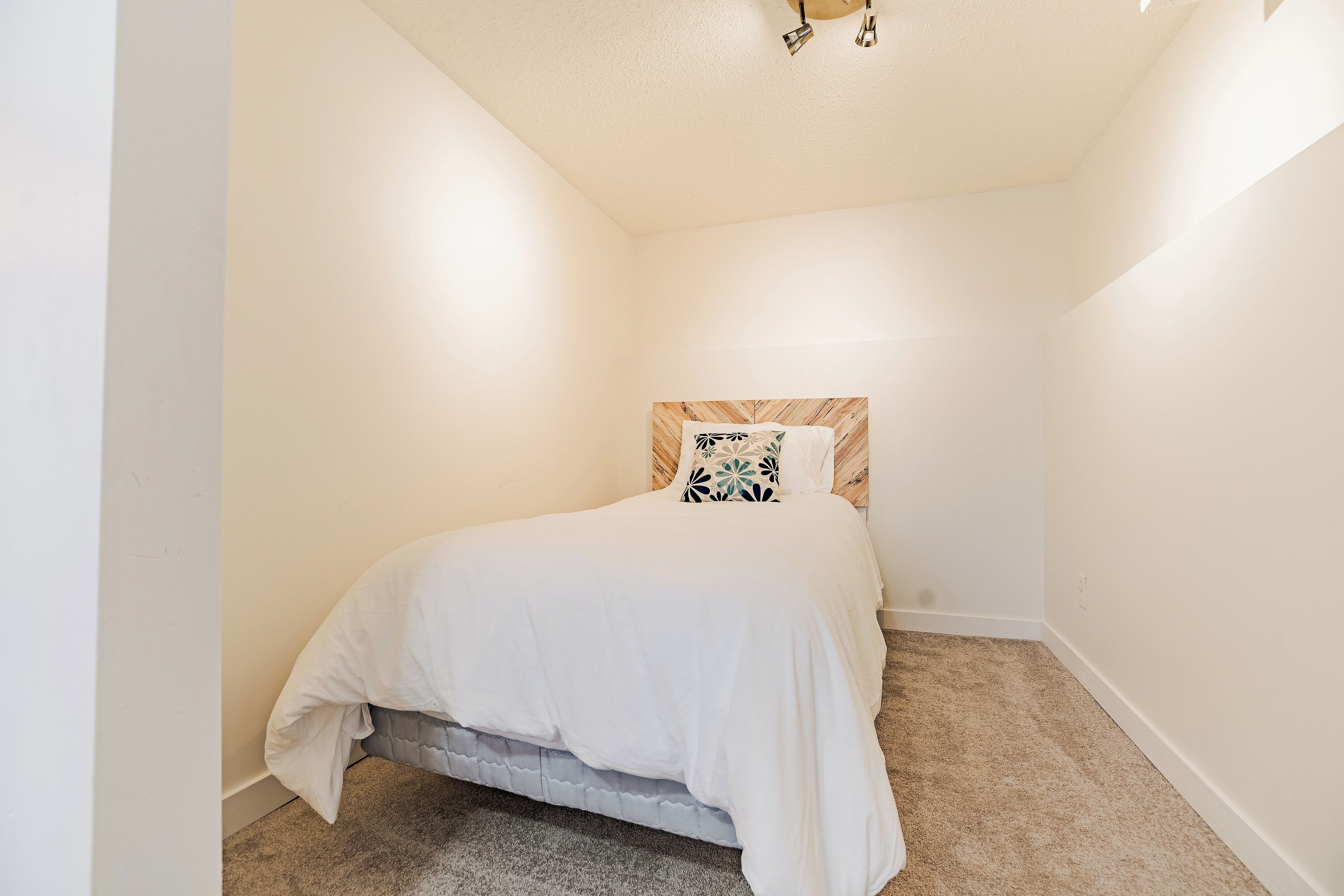 A bedroom with a single bed, a headboard with a patterned design, and a carpeted floor.