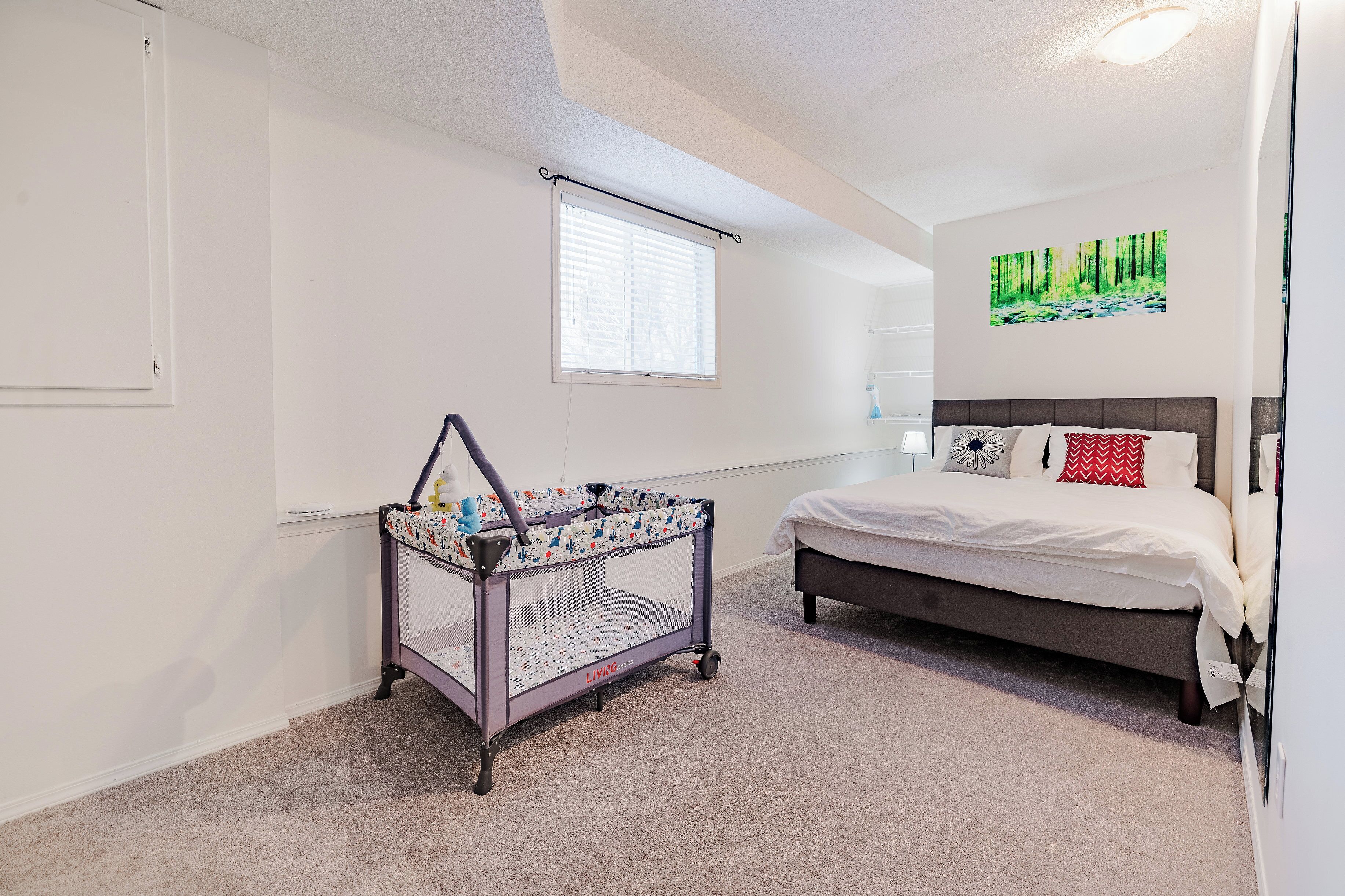 Un dormitorio con una cuna, una cama, una ventana y una obra de arte en la pared.