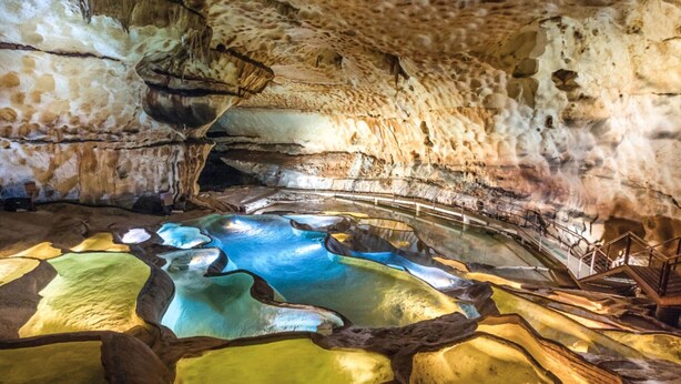 A cave interior with stalactites, a pool of water, and a wooden walkway.