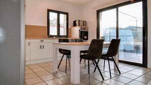 A modern kitchen with white cabinets, a dining table, and two chairs. There is a large window providing a view of the outside.