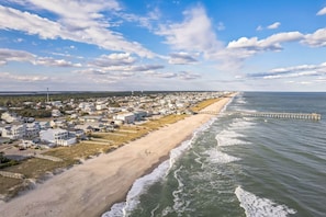 A coastal town with a beach, houses, and a pier extending into the water. - Periwinkle NEW 8 bedroom Ocean Front w/ Pool (Kure Beach)