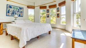 A spacious bedroom with a large bed, a ceiling fan, and multiple windows offering views of palm trees. - Secluded Beachfront Villa w/ Private Pool & Cabana (Placencia)