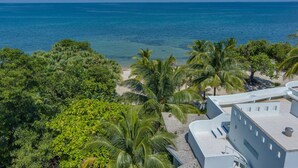 A coastal view with a beach, palm trees, and a building with a flat roof. - Secluded Beachfront Villa w/ Private Pool & Cabana (Placencia)