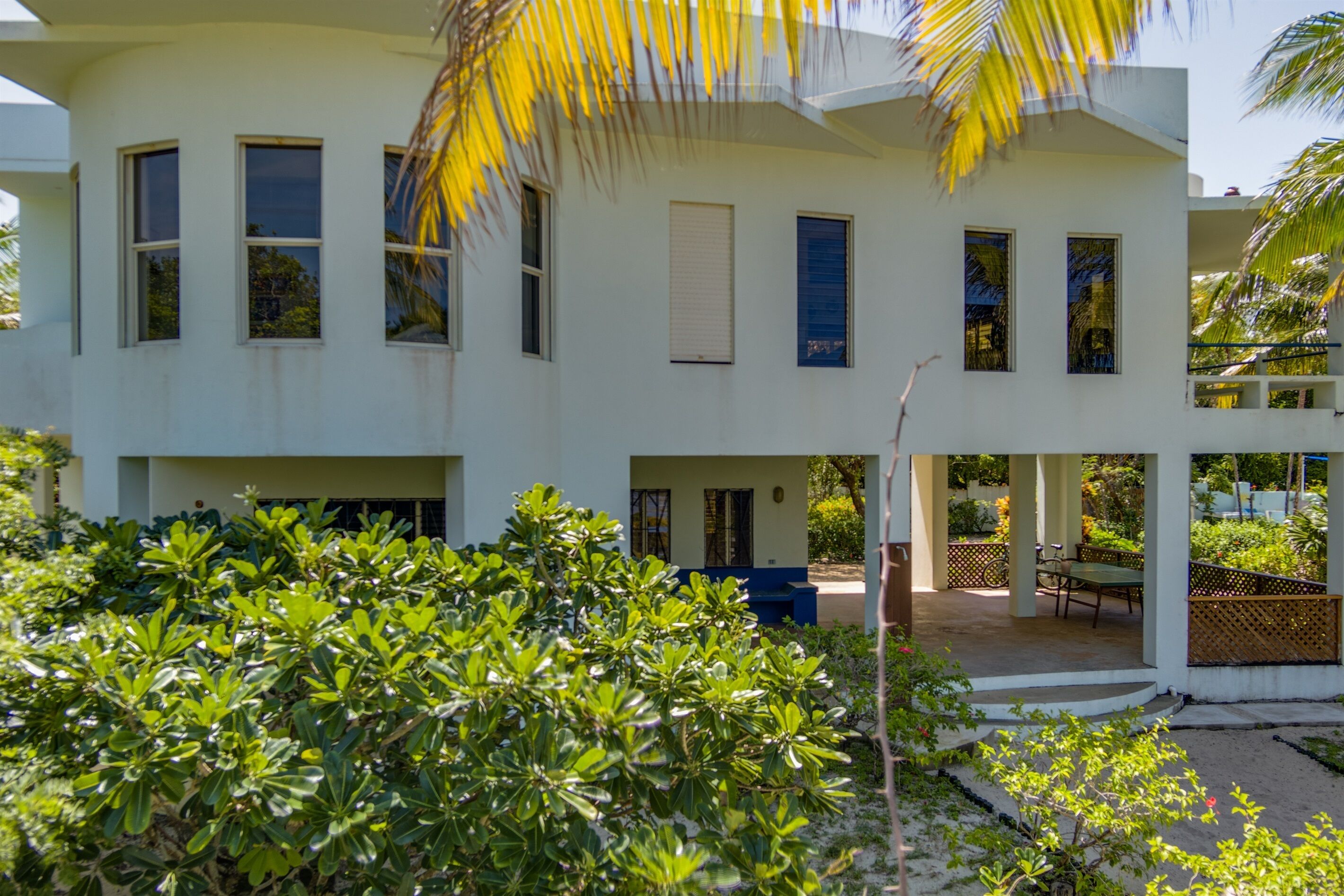 A modern two-story building with multiple windows, a covered outdoor seating area, and lush greenery in the foreground.